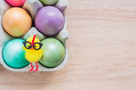 Multicolored easter eggs in a box with cute yellow chick. Top view on wooden background.の写真素材