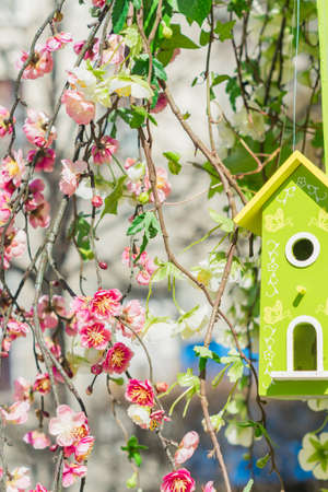 Atrificial branches of blooming cherry tree and green wooden birds house. Garden and street decorationの写真素材