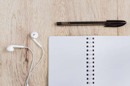 Business and office concept - blank notebook, headphones and black pen on wooden table. Minimal flat lay, top view.の写真素材