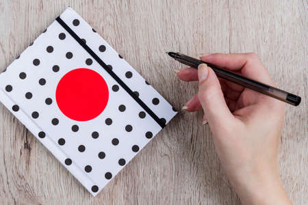 young woman hand hold black pen and polka dot cover notebook on wooden tableの写真素材