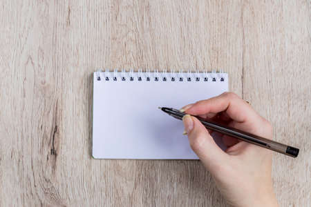 young woman hands hold opened notebook pages with black pen on wooden tableの写真素材