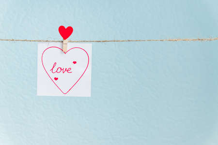 Red Valentine's love heart pin hanging on natural cord against blue background. drawn heart on paper piece.の写真素材