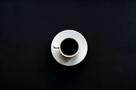 top view of white cup of coffee on black background. Minimal flat lay.の写真素材