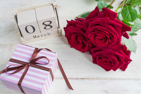 A festive gift, a wooden calendar, bouquet of red roses and a gift box on a wooden background. The concept of congratulations on March 8 or wooman's day.の写真素材
