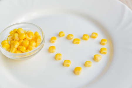 Close up of sweet corn in shape of heart on white plate.