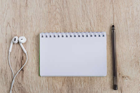 Business and office concept - blank notebook, headphones and black pen on wooden table. Minimal flat lay, top view.の写真素材