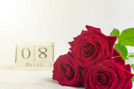 beautiful bouquet of red roses and wooden cube calendar on a wooden background. The concept of congratulations on March 8 or wooman's day.の写真素材