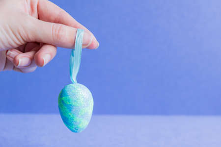 Female hand holding blue sparkling easter egg.