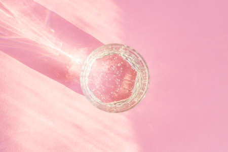 Close up of sparkling water in transparent glass and sun glare on pink background.の写真素材