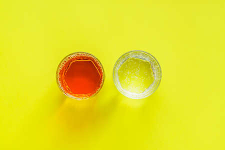 top view of transparent glasses with apple juice and sparkling water on yellow backgroundの写真素材