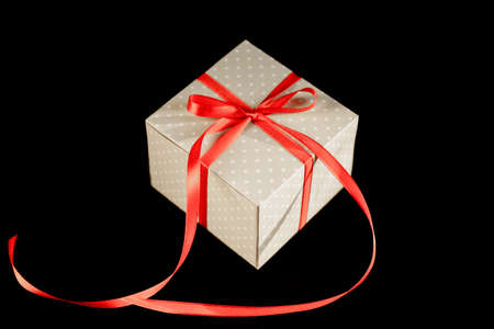 Beige polka dot gift box with red ribbon bow on black background with copy space.の写真素材