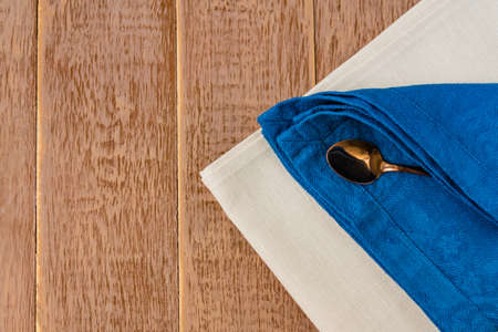 Top view of cloth napkins of beige, blue colors and served tea spoon on wooden table.の写真素材