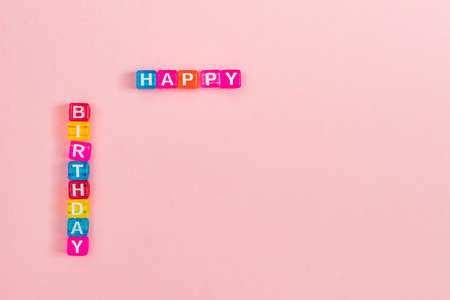 Happy birthday inscription made of colorful cube beads with letters. Festive pink background concept...