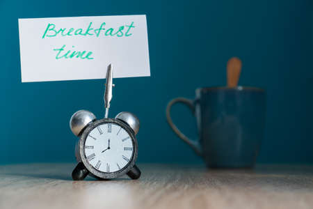 Alarm clock and banner with handwritten phrase "breakfast time" on wooden table. Time management concept.の写真素材