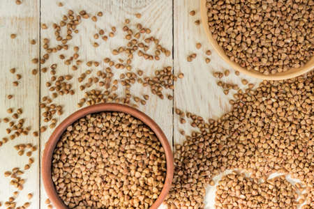 Dry buckwheat in brown clay bowl on wooden table. gluten free grain for healthy dietの写真素材