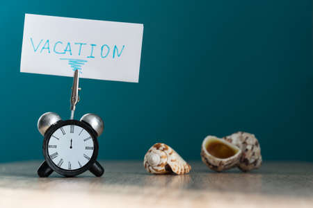 Alarm clock and banner with handwritten phrase vacation on wooden table. Vacation concept.