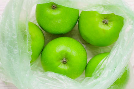 Fresh green apples in plastic bag on wooden table. environmental concept of non-ecological use of plasticの写真素材
