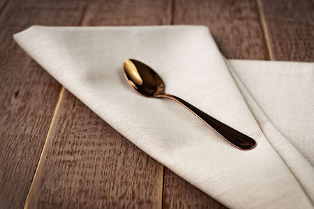 Close up of textile beige napkin and served tea spoon on wooden table.の写真素材