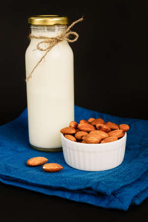Homemade Almond milk in a bottle and glass with nuts in white porcelain bowl on black background.の写真素材