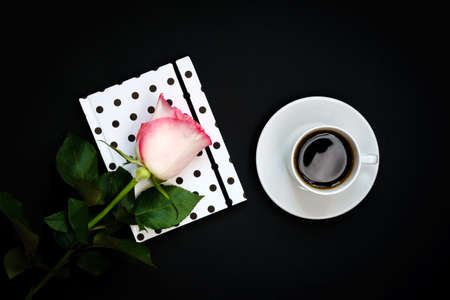 Cup of black coffee, notebook and pink rose on black background, Top view, copy space.の写真素材