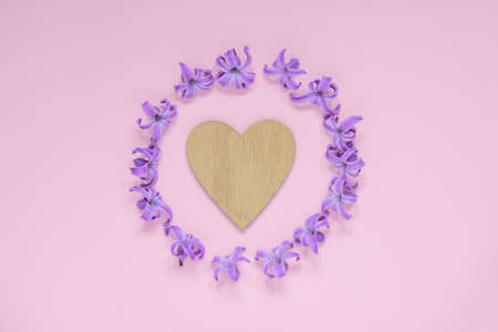 Round frame of pastel purple hyecinth flowers and wooden heart on gradient pink background. Floral...