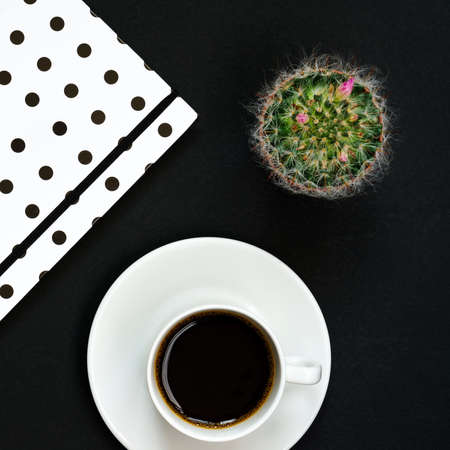 Cup of black coffee, notebook and blooming cactus on black background, Top view, copy space.の写真素材
