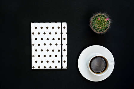 Cup of black coffee, notebook and blooming cactus on black background, Top view, copy space.の写真素材