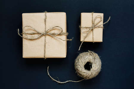 Handcrafted gift box wrapped in Craft paper with rope and bow on black background. Top view, flat layの写真素材