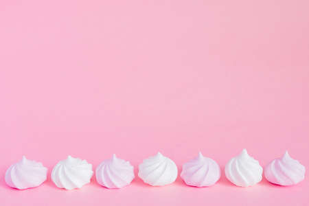 white and pink twisted meringues in a row on pink background, greeting card, copy space