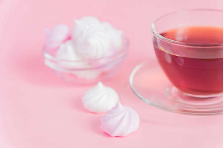 White and pink twisted meringues and cup of tea on pink background. French dessert prepared from whipped with sugar and baked egg whites. Greeting card with copy spaceの写真素材
