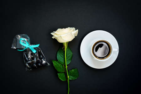 Cup of black coffee, chocolate sweets and white rose on black background, Top view, copy space. Toned imageの写真素材