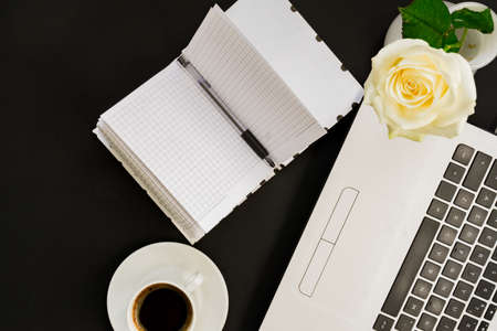 Flat lay, top view office table desk. Workspace with laptop, white rose, open diary and coffee mug on black background.の写真素材
