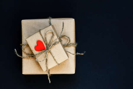 Handcrafted gift box wrapped in Craft paper with red wooden heart, rope and bow on black background....