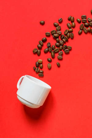 Top view of fresh roasted coffe beans and whte cup on red background. Flat lay.