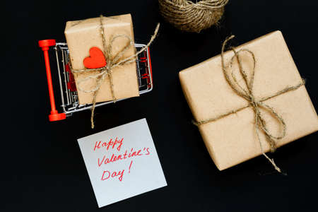 Handcrafted gift box wrapped in Craft paper with red wooden heart, rope and bow on black background. Top view, flat layの写真素材