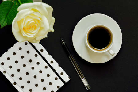 Cup of black coffee, notebook and white rose on black background, Top view, copy space.の写真素材