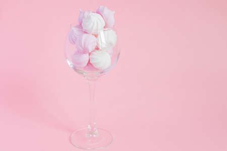 White and pink twisted meringues in a vine glass on pink background. French dessert prepared from...