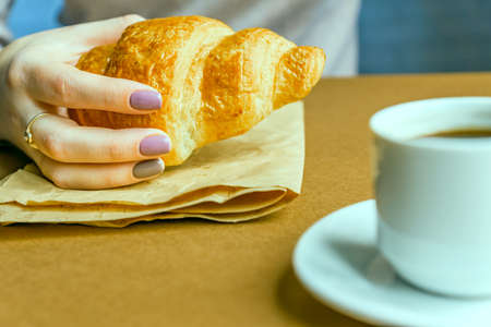 Female hands with manicure holding croissant. Breakfast in french style