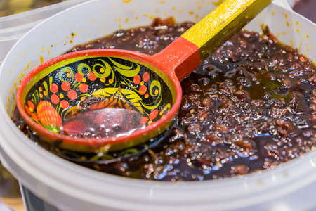close up of tasty berry jam in plastic bowl and woden hohloma style scoop.