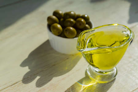 glass sauceboat with extra virgin olive oil and fresh green olives on wooden table.の写真素材