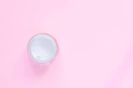 glass jar with face or body cream on pastel pink background with copy space. Top view, flat lay.