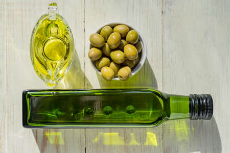 glass sauceboat with extra virgin olive oil, fresh green olives and bottle on wooden table.の写真素材