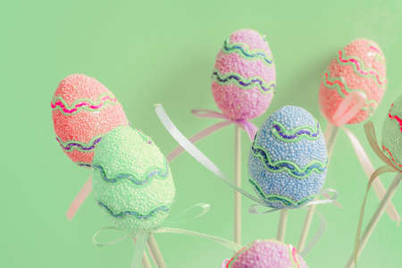 Easter colorful decorated eggs stand on a sticks on pastel green background. Minimal easter concept....