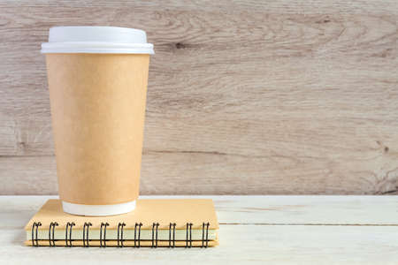 craft paper coffee cup and notebook diary with copy space on wooden table in minimalism styleの写真素材