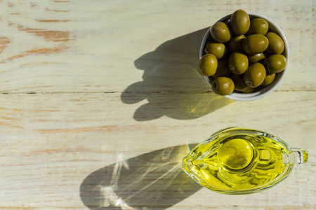 Top view of glass sauceboat with extra virgin olive oil and fresh green olives on wooden table.の写真素材