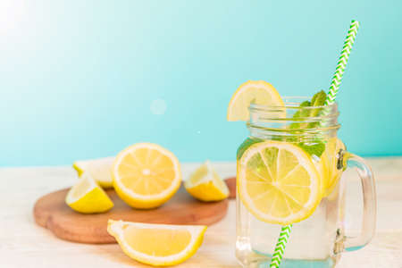 Mason jar glass of homemade lemonade with lemons, mint and green paper straw on wooden rustic background. Summer refreshing beverage.の写真素材
