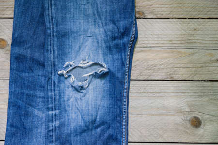 top view of blue faded jeans with a hole on wooden background. Beauty, fashion and shopping concept....
