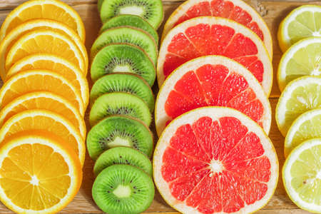 close up of slices of oranges, lemons, kiwi, grapefruit pattern on wooden background.の写真素材