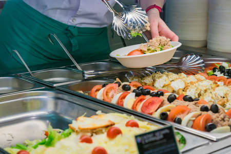 buffet self-service food display human hand take plate and put a salad. full lunch service stationの写真素材