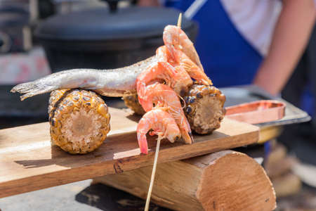 chef serves wooden desk with seafood and sweet grilled corn at the festival. Street food prepared on...